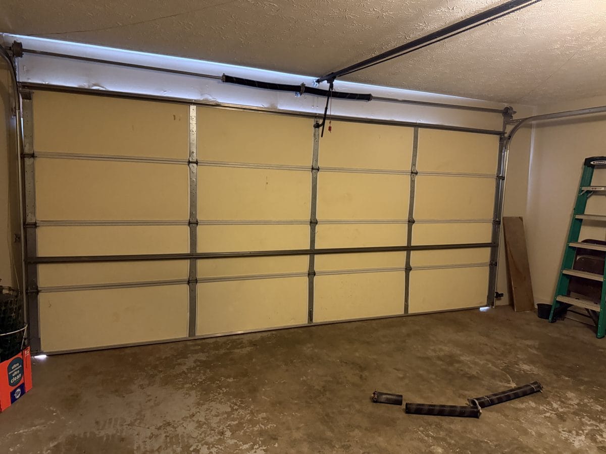 Double garage door after torsion spring replacement, with the broken spring on the floor